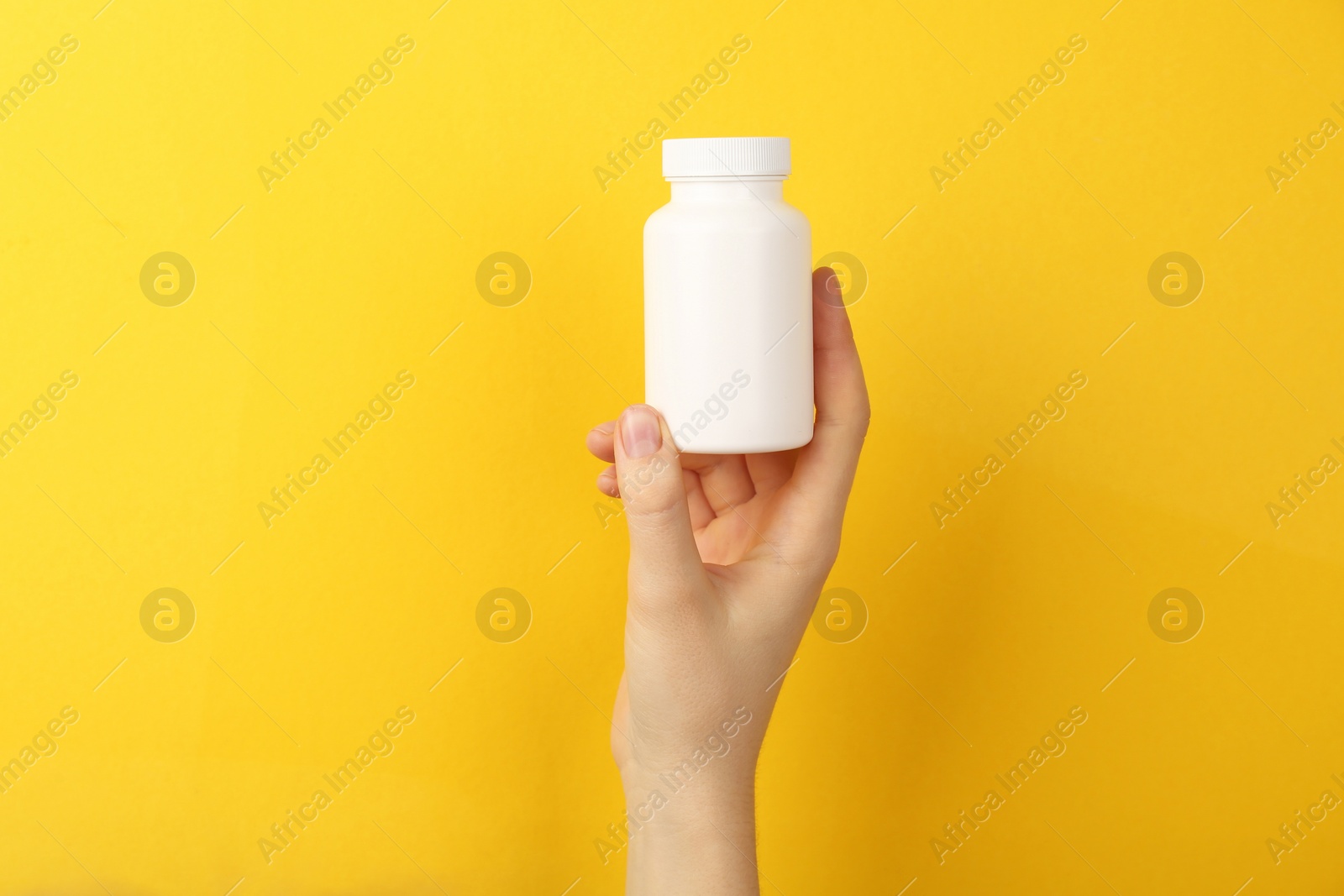 Photo of Woman holding blank white jar of vitamins on yellow background, closeup. Space for text