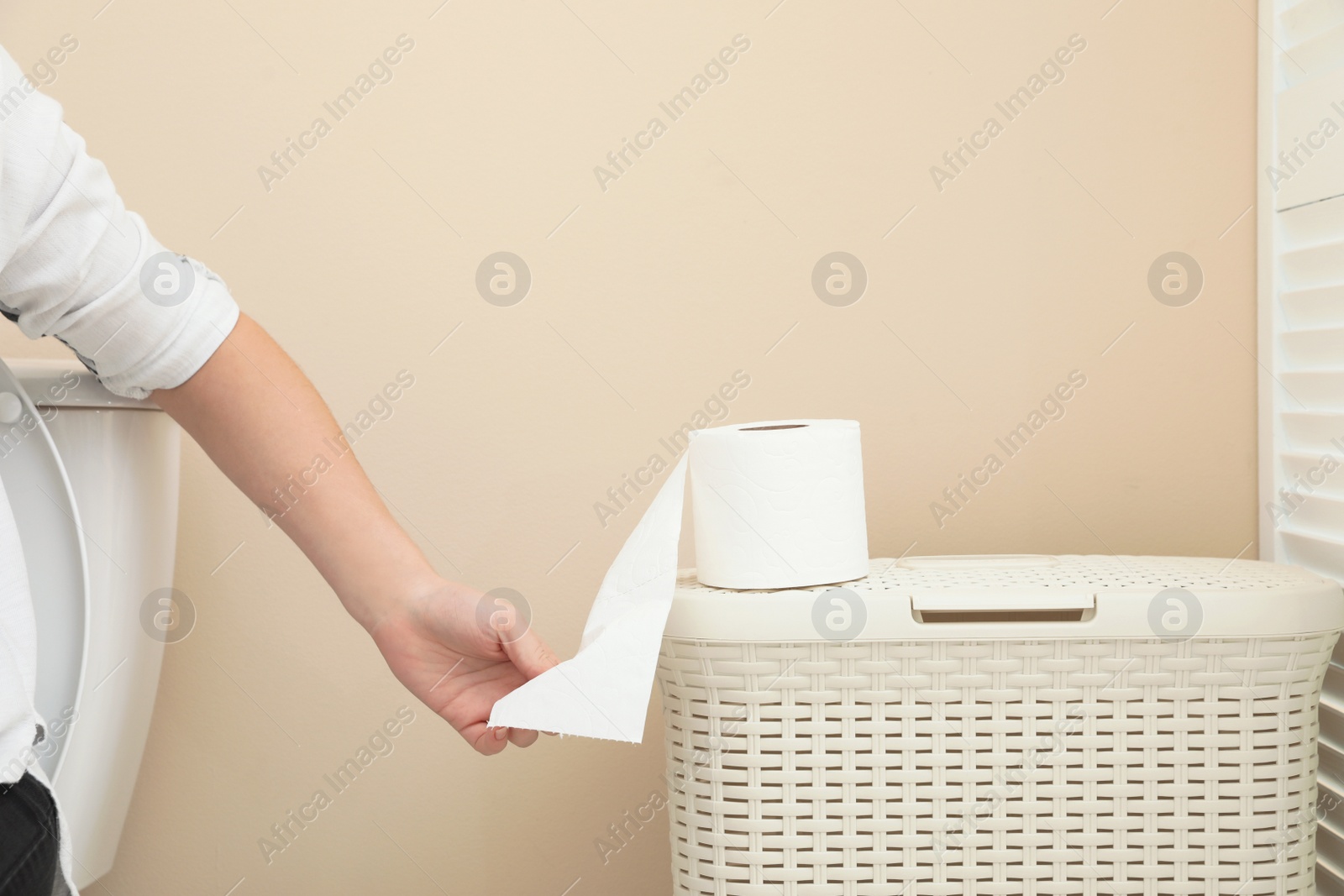 Photo of Woman taking toilet paper from roll in bathroom, closeup