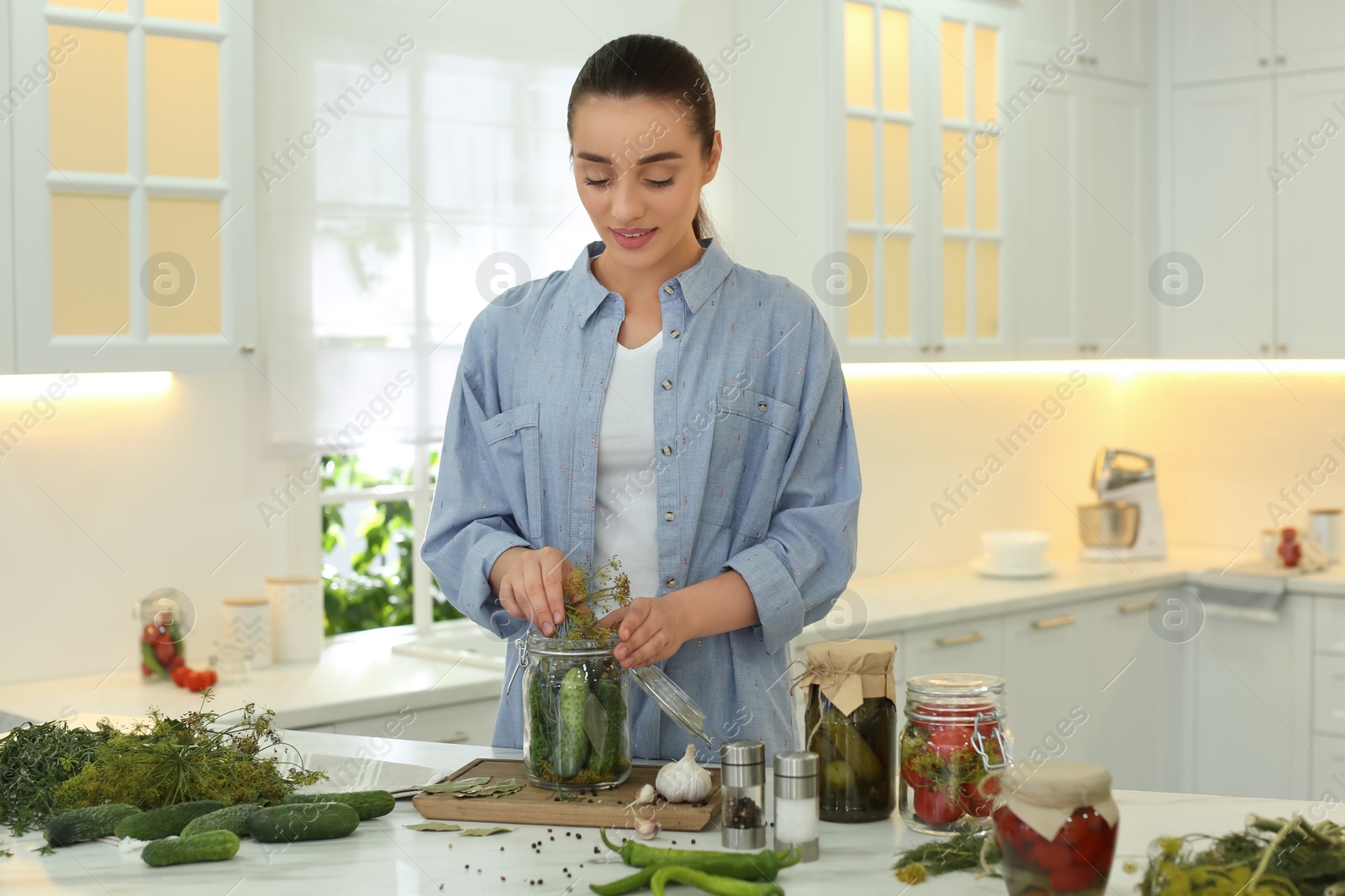Photo of Woman putting dill into pickling jar at table in kitchen