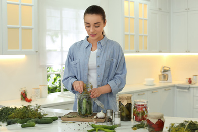 Woman putting dill into pickling jar at table in kitchen