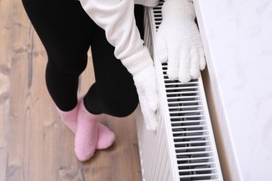 Photo of Girl warming hands on heating radiator indoors, closeup