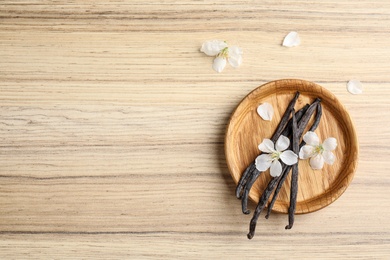Photo of Flat lay composition with aromatic vanilla sticks and flowers on wooden background, space for text