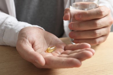 Photo of Man with glass of water and pill at wooden table, closeup