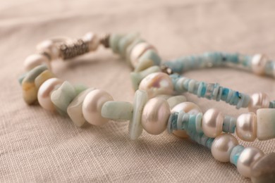 Photo of Beautiful necklace with gemstones on light cloth, closeup