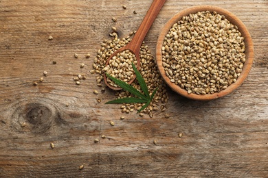 Photo of Organic hemp seeds and leaf on wooden background, flat lay. Space for text