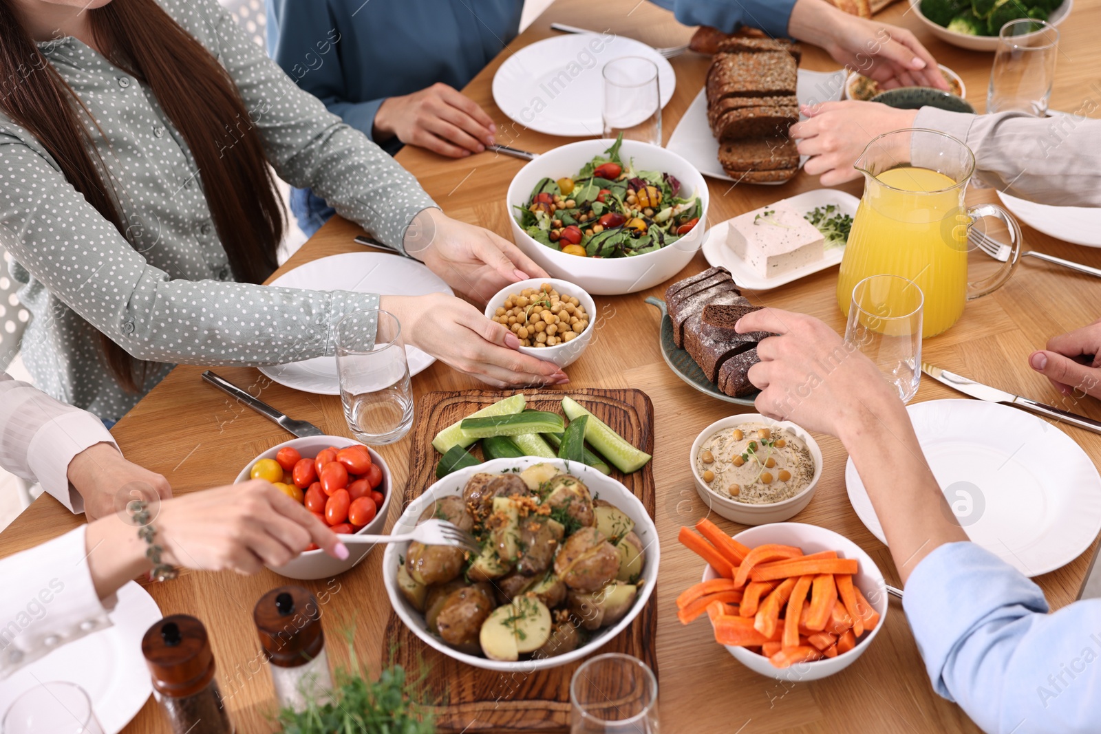 Photo of Friends eating vegetarian food at wooden table indoors, closeup