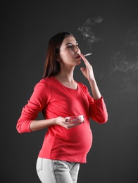 Photo of Pregnant woman smoking cigarette on black background