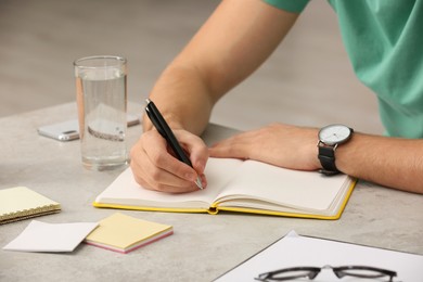 Man writing in notebook at table indoors, closeup