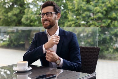 Photo of Handsome bearded man adjusting cufflinks in outdoor cafe