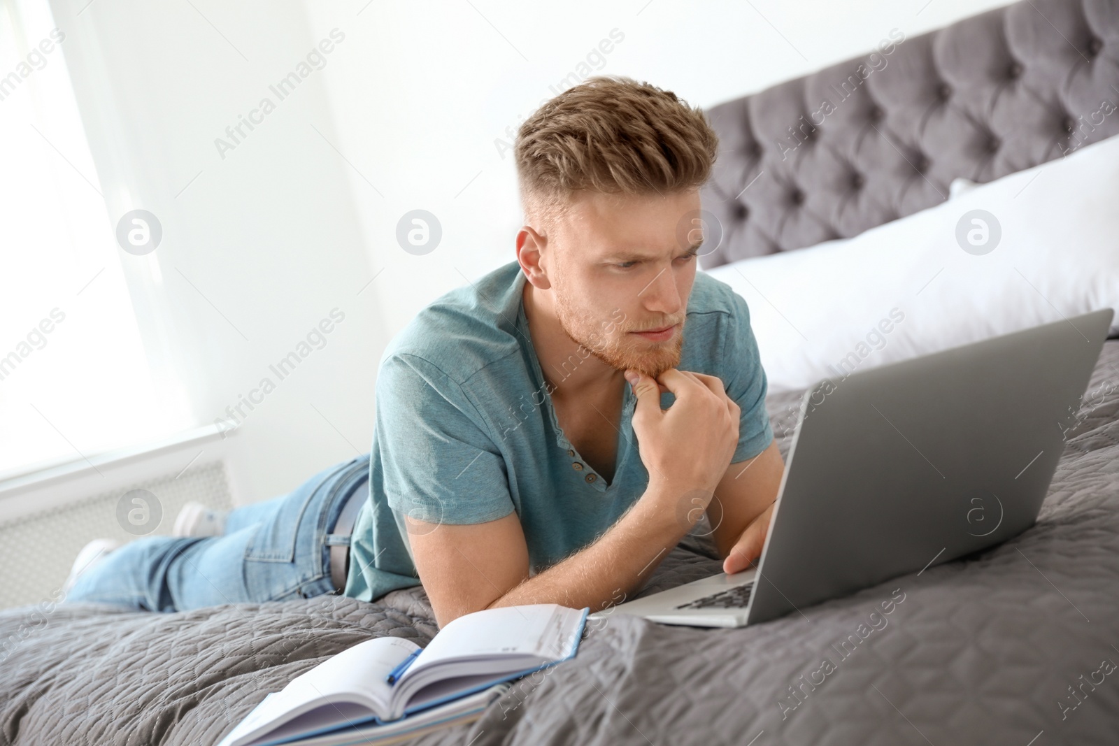 Photo of Young man using laptop while lying on bed at home