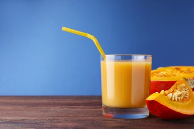 Photo of Tasty pumpkin juice in glass and cut pumpkin on wooden table against blue background. Space for text