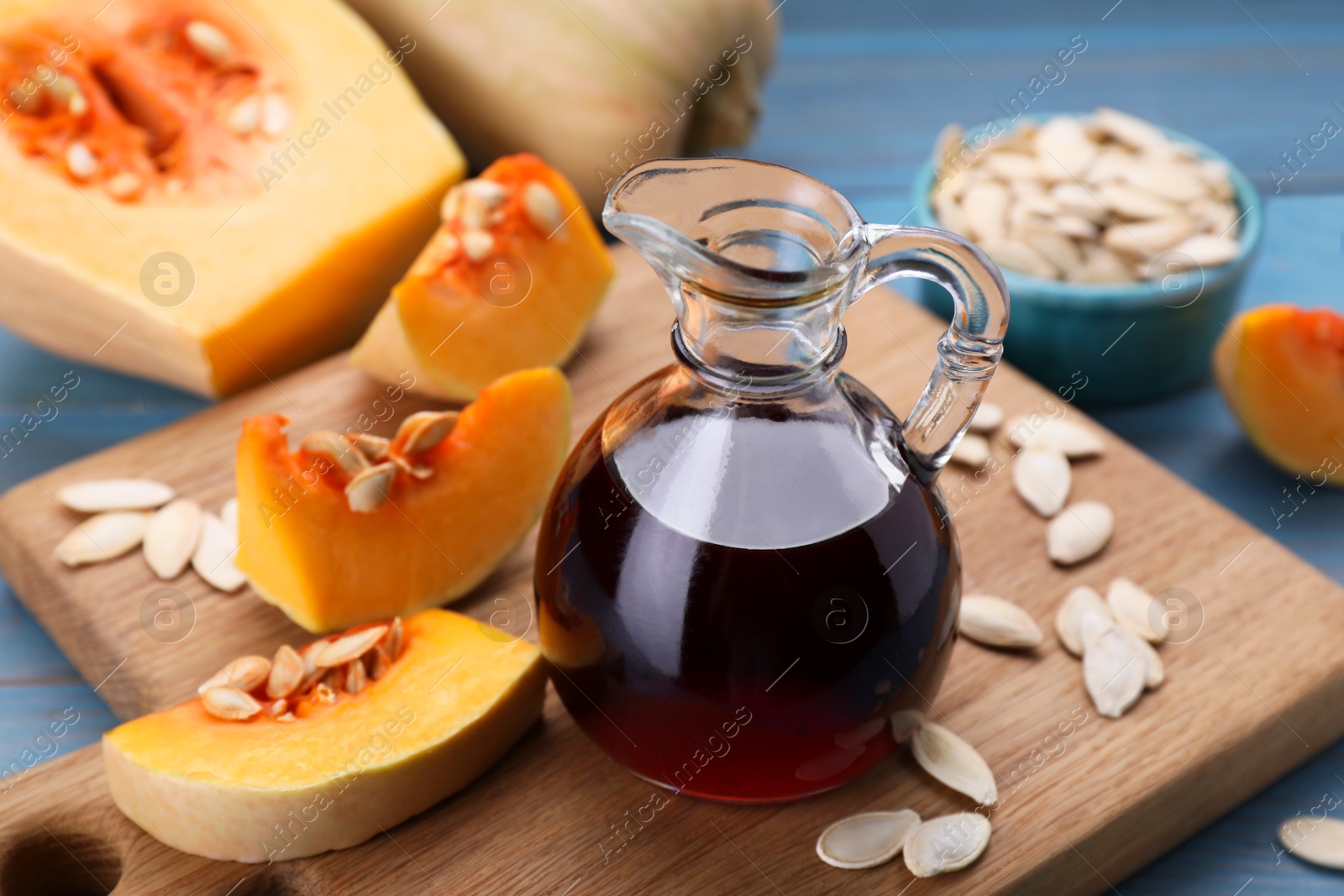 Photo of Fresh pumpkin seed oil in glass jug on blue wooden table