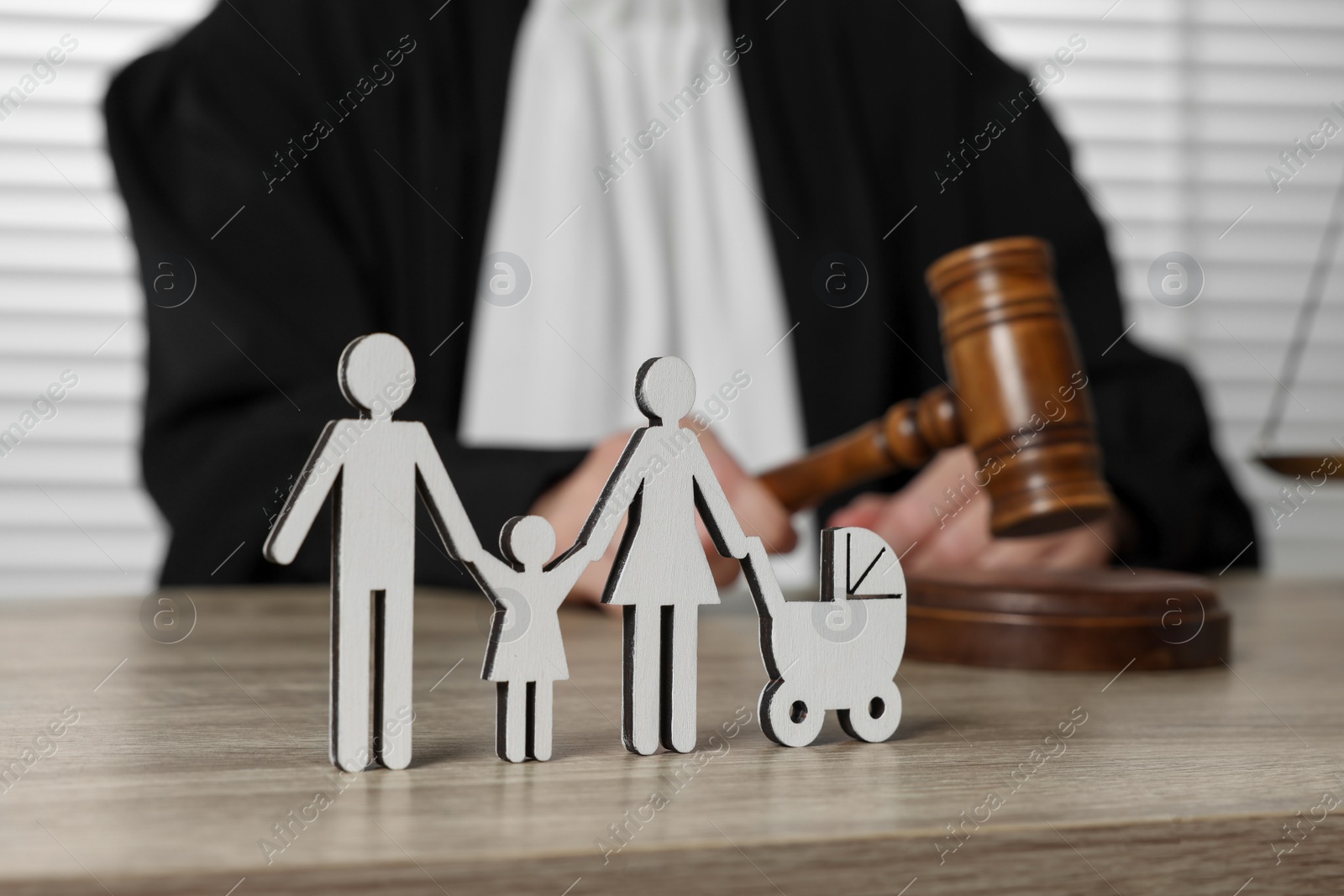 Photo of Family law. Judge with gavel sitting at wooden table, focus on figure of parents and children