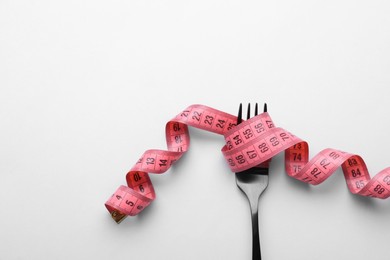 Fork with measuring tape on white background, top view with space for text. Diet concept