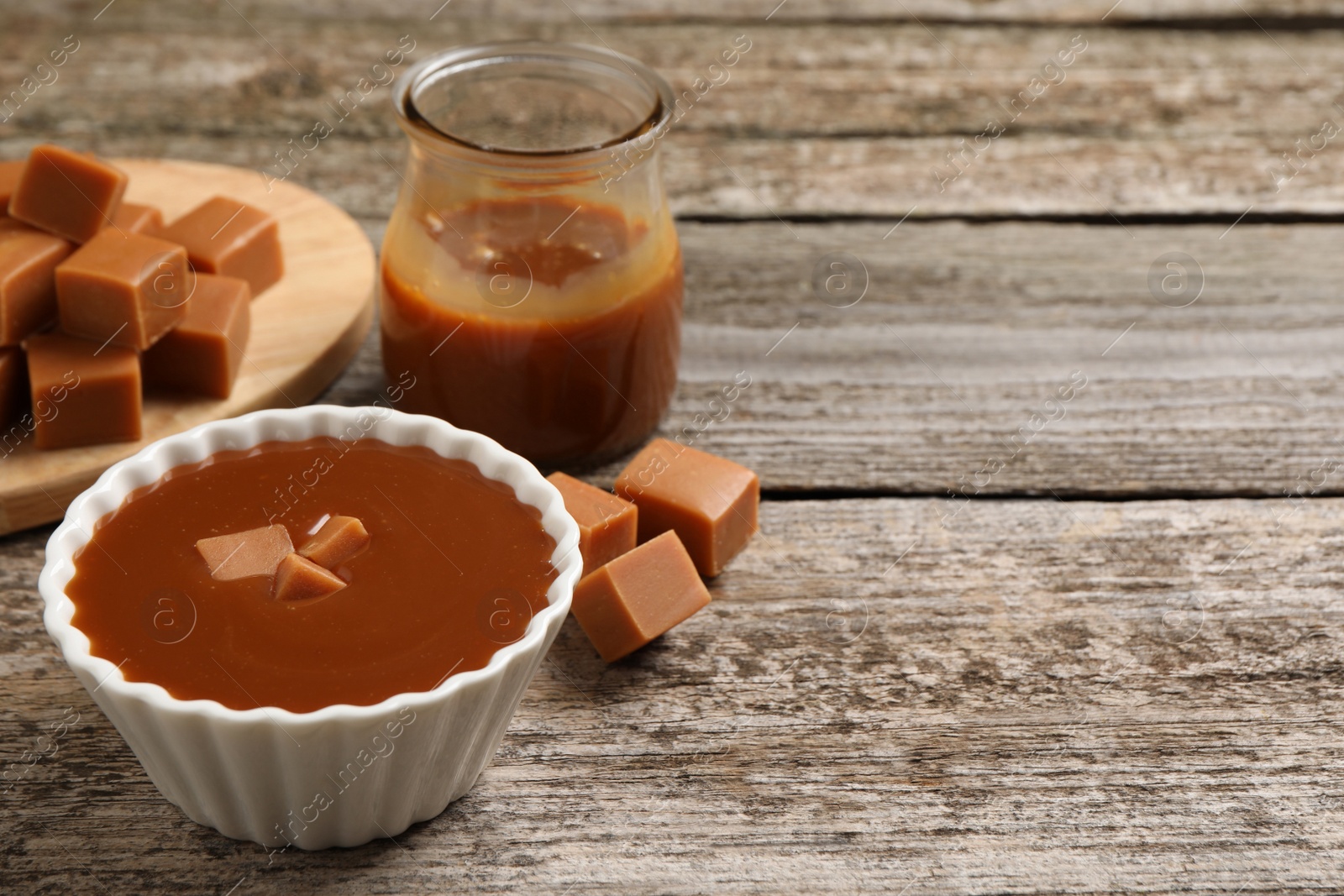 Photo of Tasty salted caramel and candies on wooden table, space for text