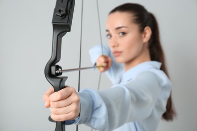 Young woman practicing archery against light grey background, focus on bow