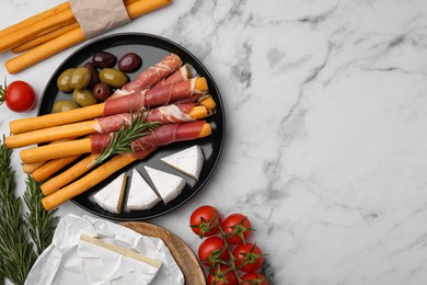 Photo of Delicious grissini sticks with prosciutto and ingredients on white marble table, flat lay. Space for text