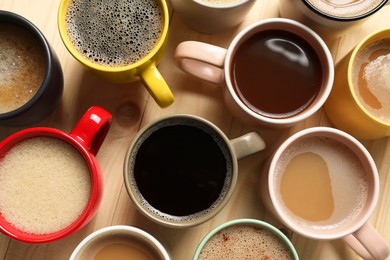 Photo of Many cups with different aromatic coffee on wooden table, flat lay