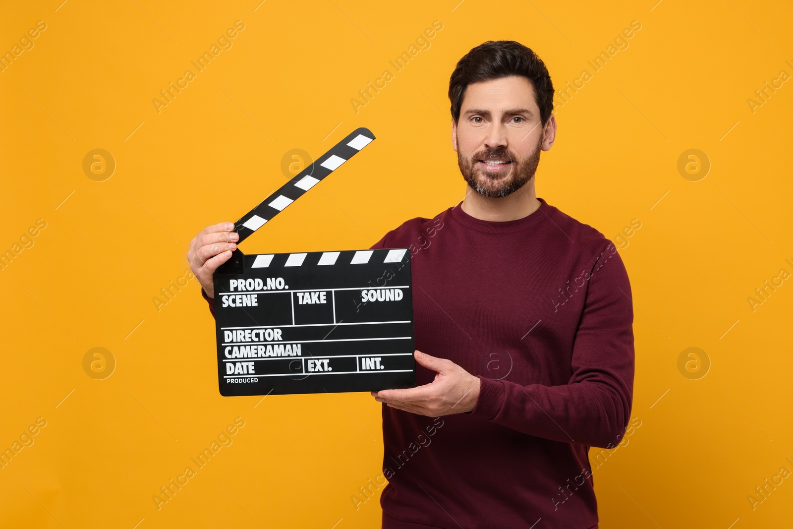 Photo of Smiling actor holding clapperboard on orange background