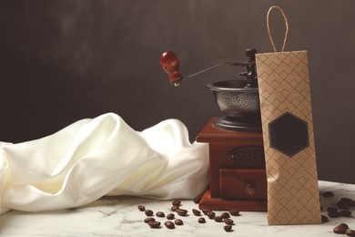 Photo of Scented sachet, coffee grinder and beans on white marble table against black background, space for text