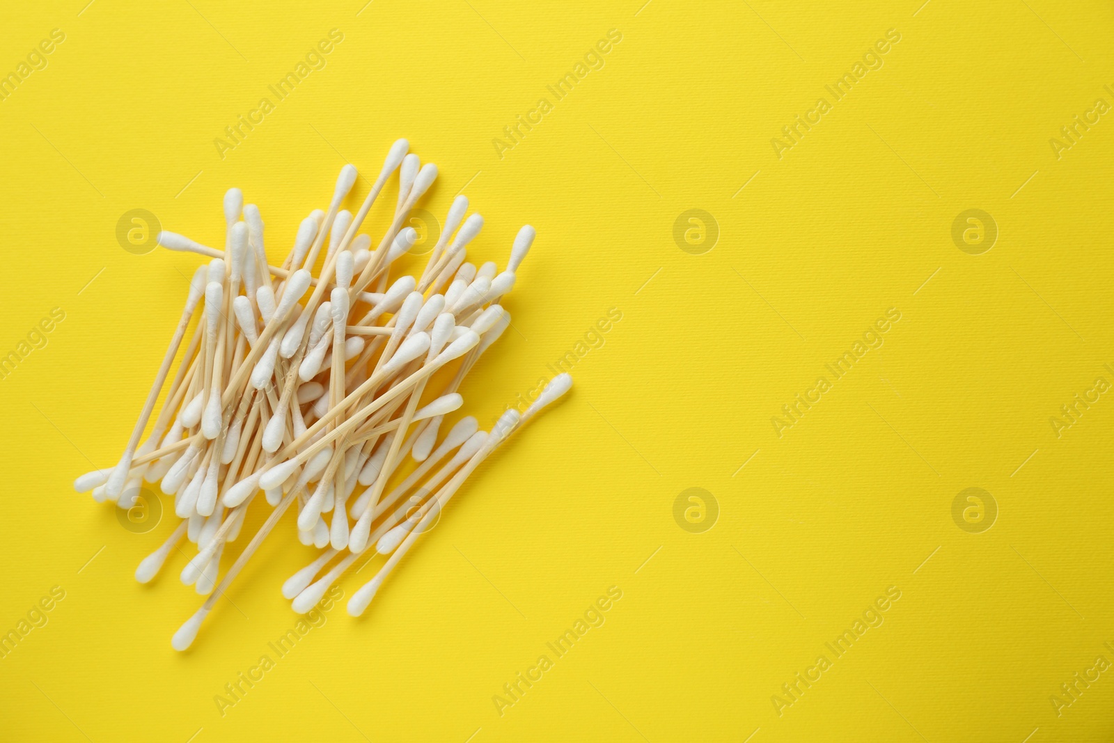 Photo of Heap of wooden cotton buds on yellow background, flat lay. Space for text