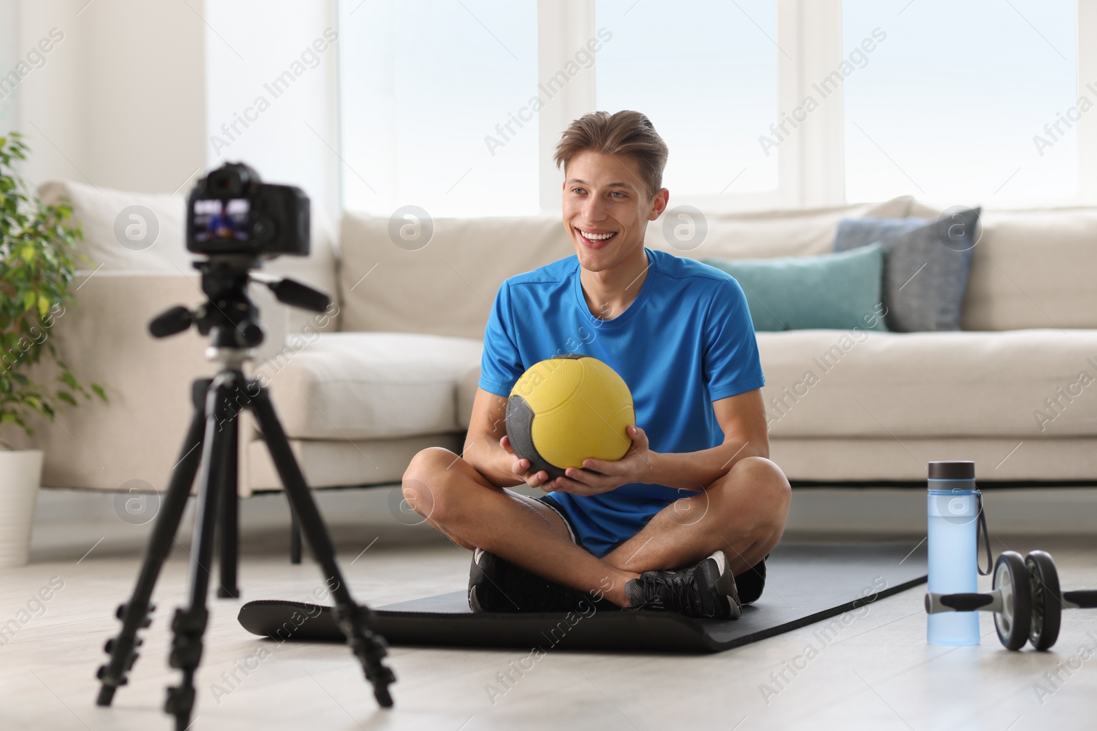 Photo of Smiling sports blogger holding medicine ball while recording fitness lesson with camera at home