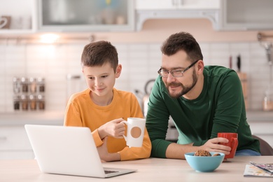 Photo of Little boy and his dad using laptop in kitchen
