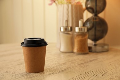 Takeaway paper cup with coffee on wooden table indoors. Space for text