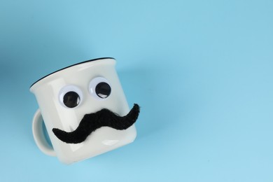 Photo of Man's face made of cup, fake mustache and decorative eyes on light blue background, top view. Space for text