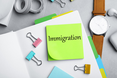 Note with word IMMIGRATION and stationery on grey grey table, flat lay