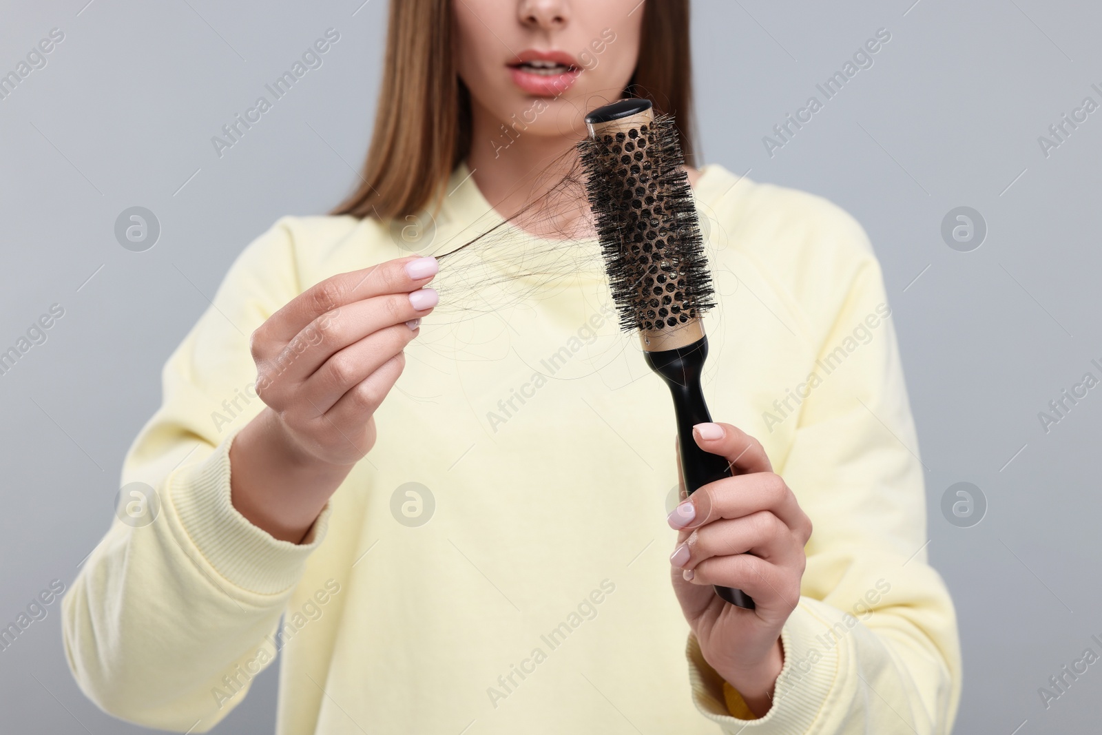 Photo of Woman untangling her lost hair from brush on light grey background, closeup. Alopecia problem