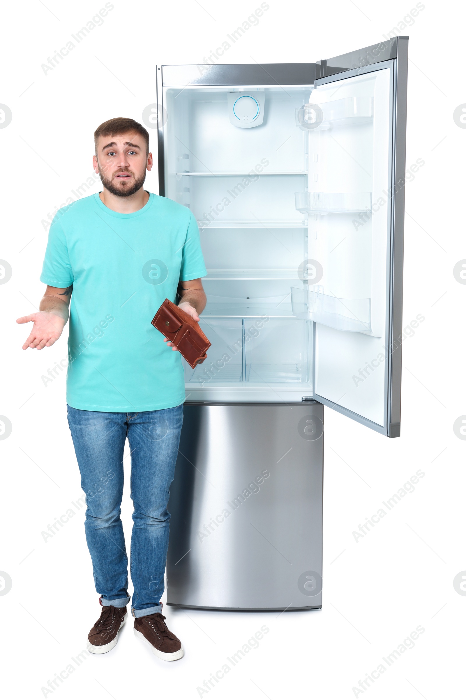 Photo of Young man with no money in wallet near empty refrigerator on white background