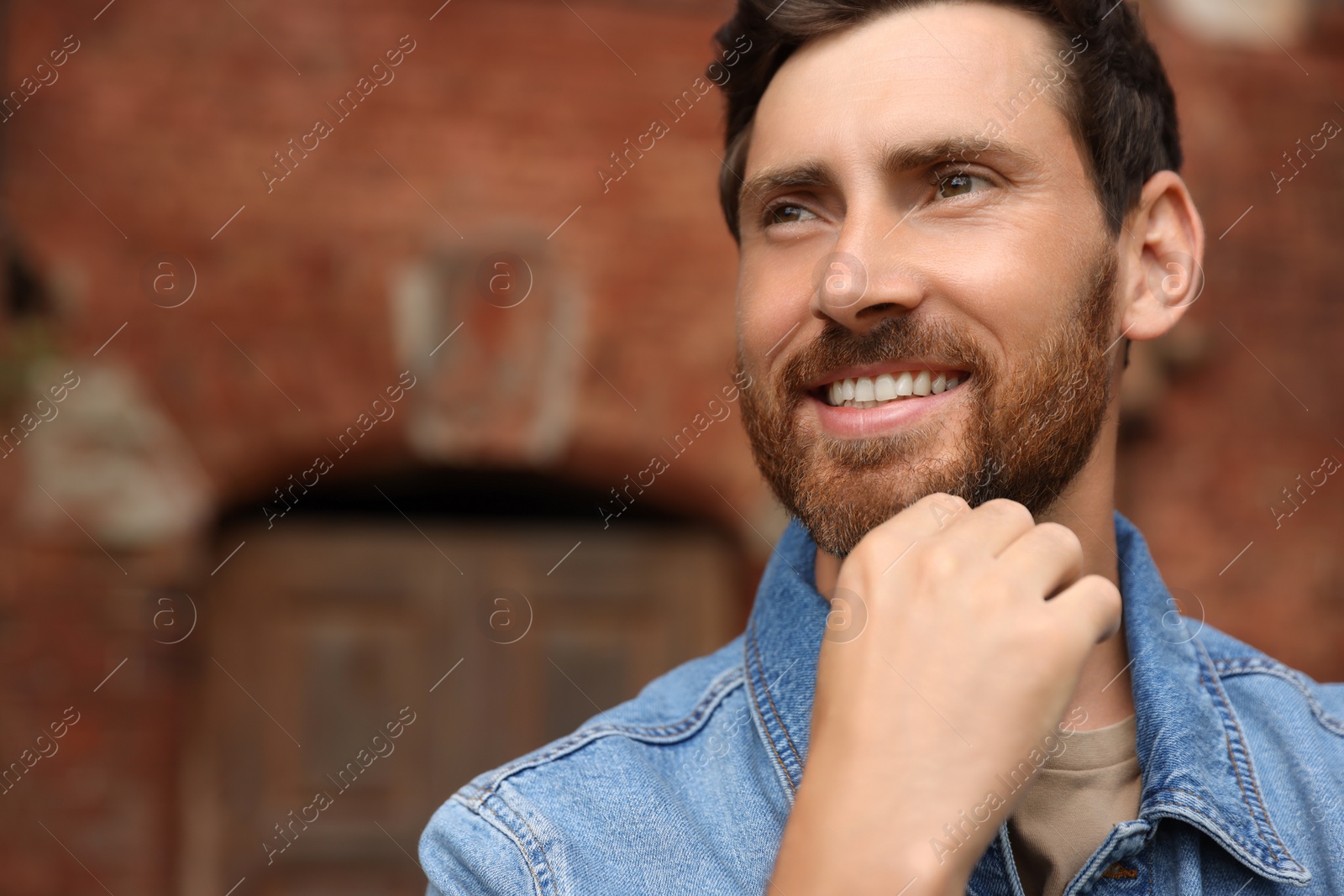 Photo of Smiling handsome bearded man looking away outdoors. Space for text