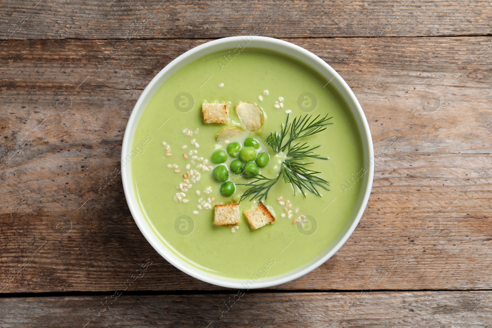 Photo of Fresh vegetable detox soup made of green peas with croutons in dish on wooden background, top view