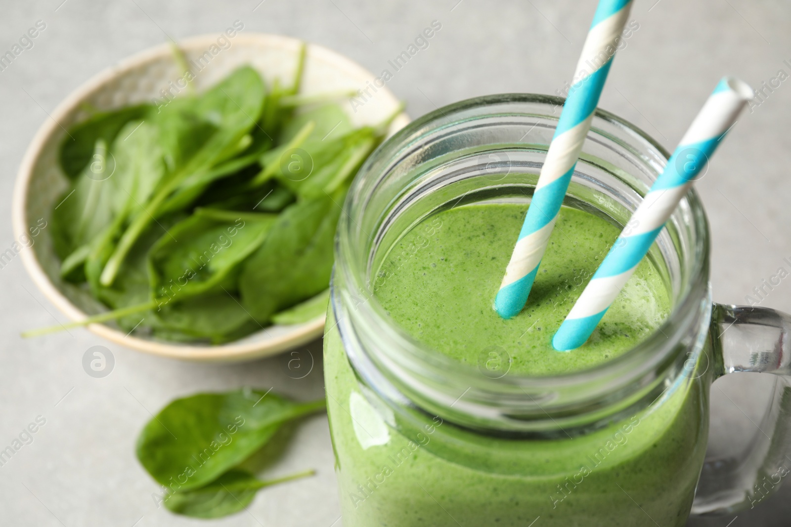 Photo of Mason jar of healthy green smoothie with fresh spinach on grey table, closeup view