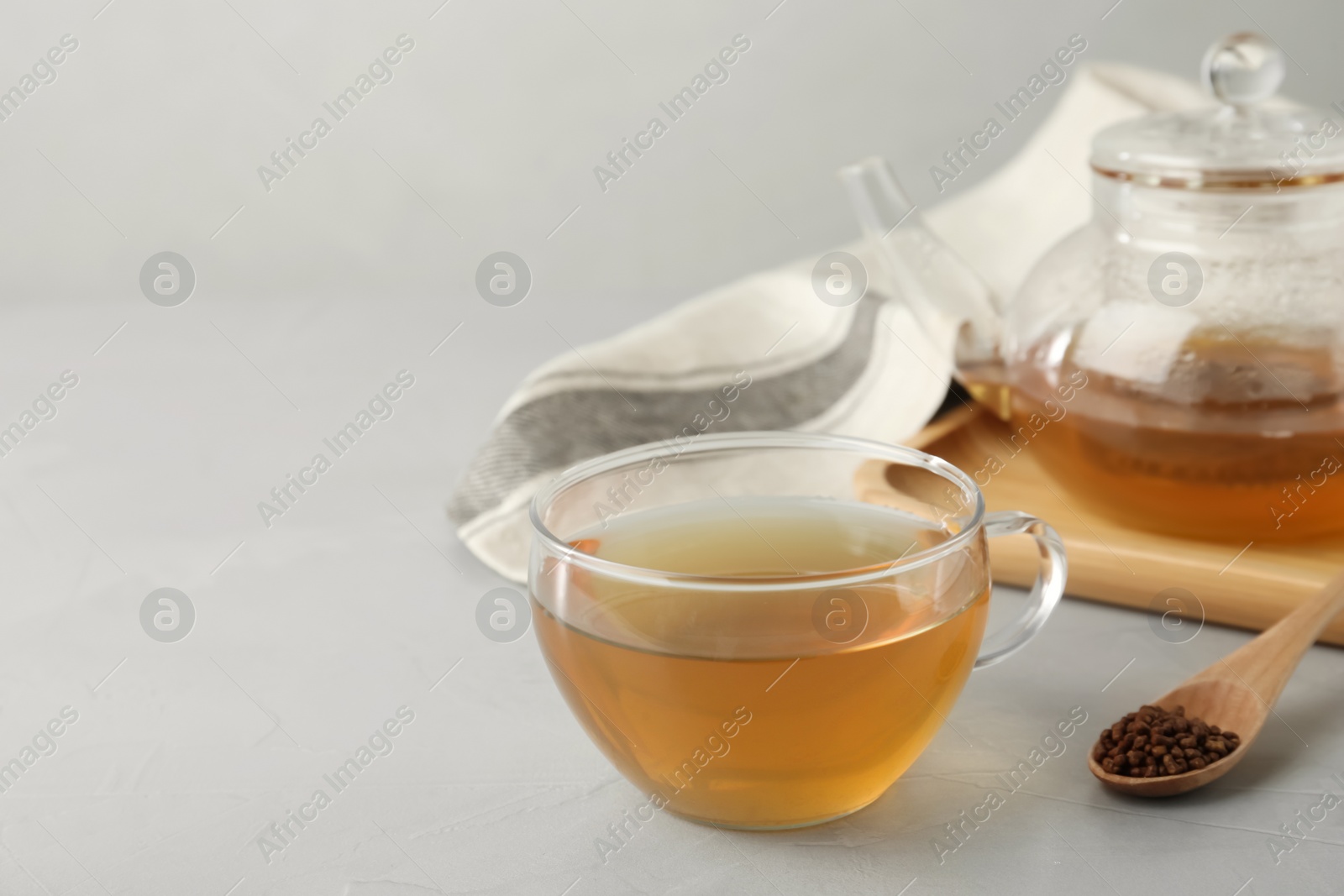 Photo of Glass cup of buckwheat tea and granules on light grey table. Space for text