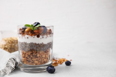 Photo of Tasty granola with berries, nuts, yogurt and chia seeds in glass on light table, space for text