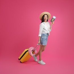 Happy female tourist with suitcase, ticket and passport on pink background