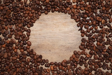 Photo of Frame made of roasted coffee beans on wooden table, flat lay. Space for text