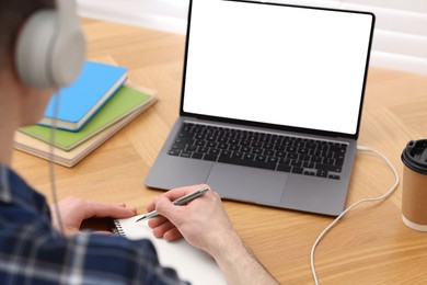 Photo of E-learning. Man taking notes during online lesson at table indoors, closeup