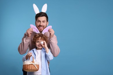 Photo of Happy father and son in cute bunny ears having fun on light blue background. Space for text. Easter celebration