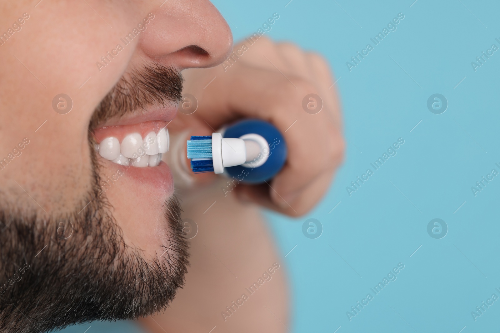 Photo of Man brushing his teeth with electric toothbrush on light blue background, closeup. Space for text