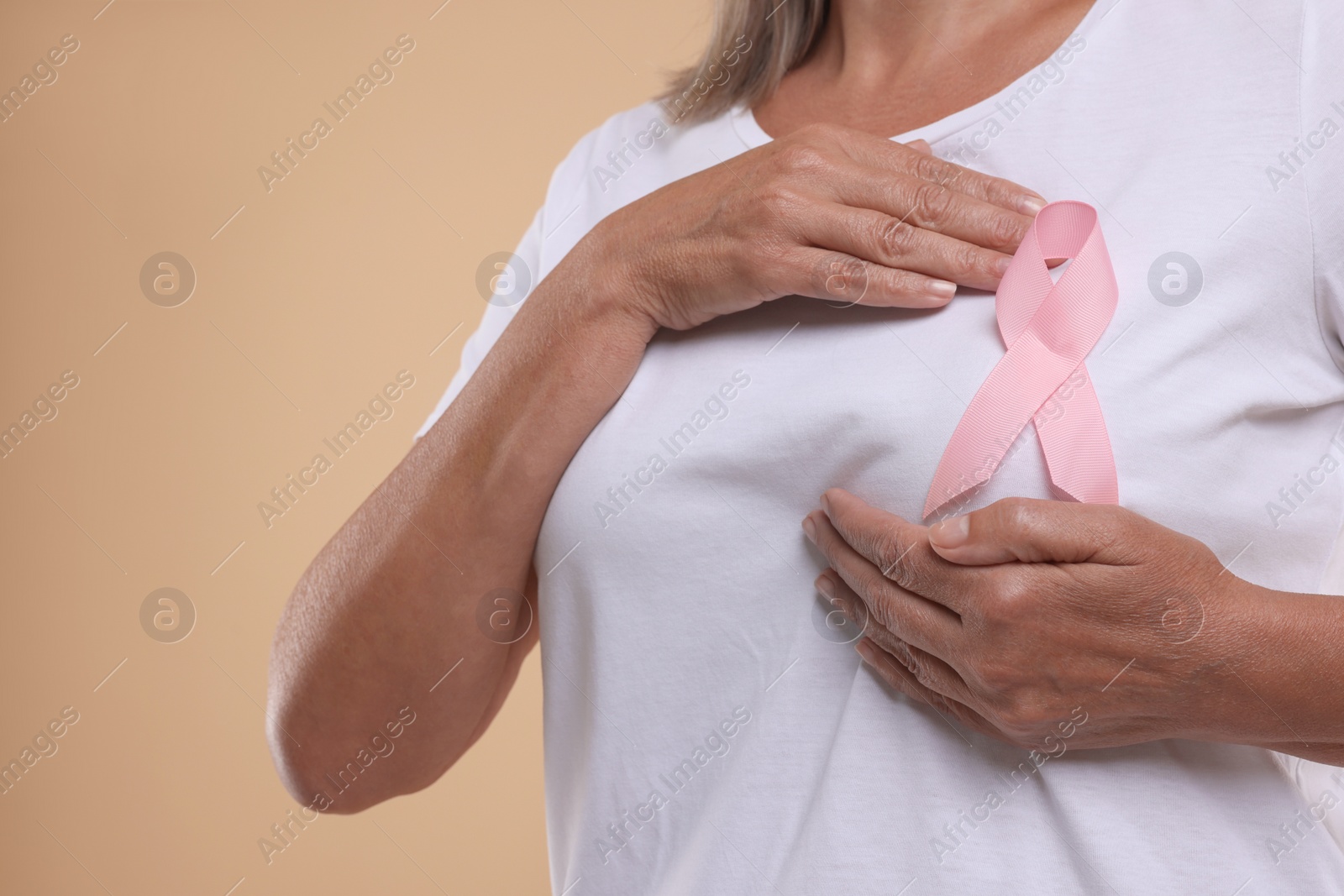 Photo of Breast cancer awareness. Woman with pink ribbon doing self-examination on light brown background, closeup. Space for text