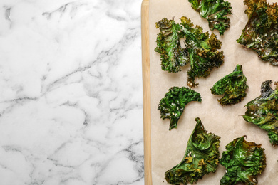 Photo of Tasty baked kale chips on marble table, top view. Space for text