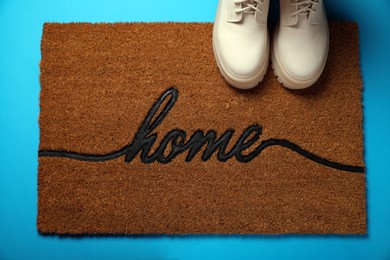 Doormat with word Home and stylish boots on light blue background, flat lay