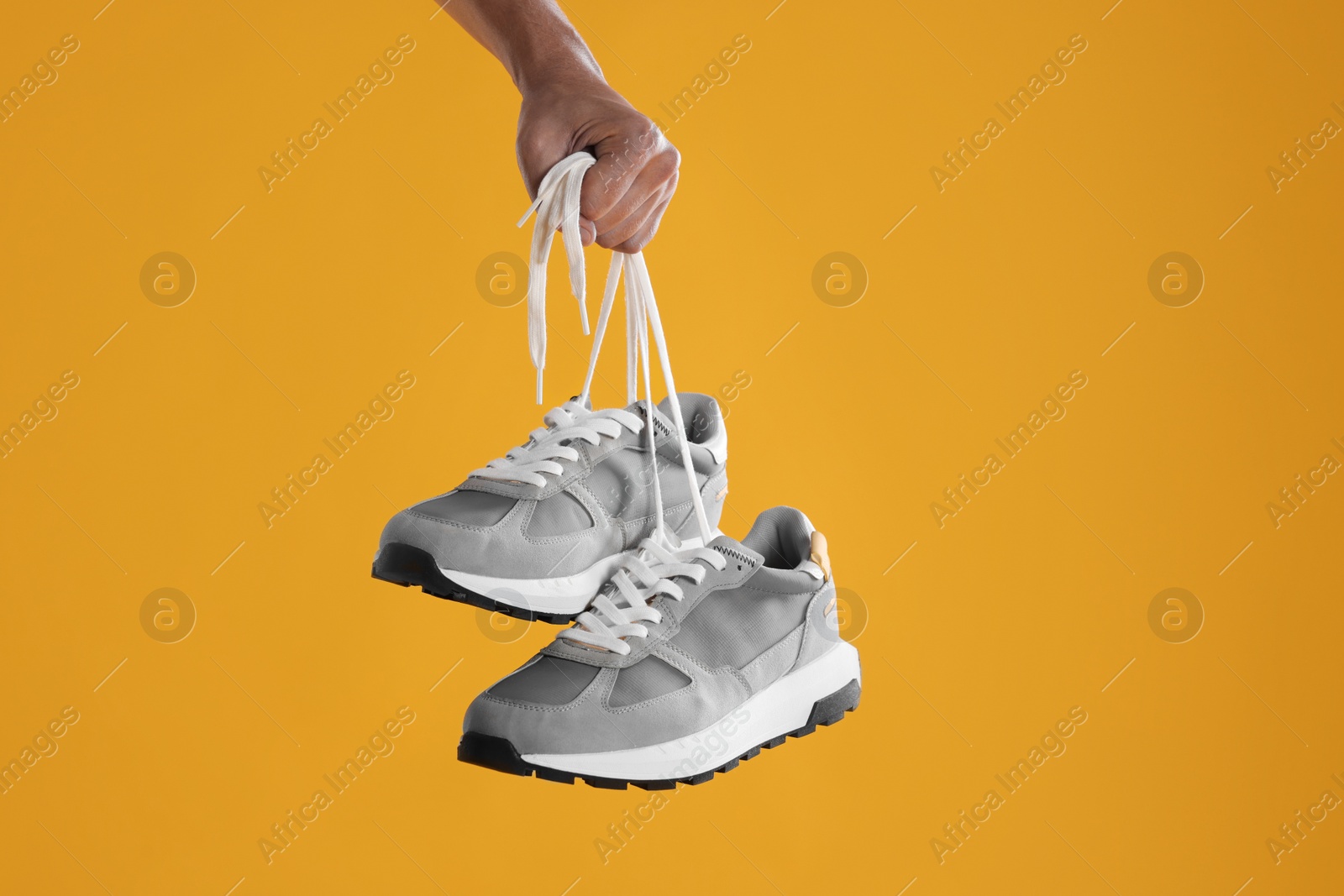 Photo of Man holding stylish sneakers on yellow background, closeup