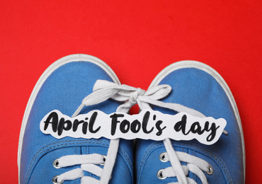 Photo of Shoes tied together and note with phrase APRIL FOOL'S DAY on red background, top view