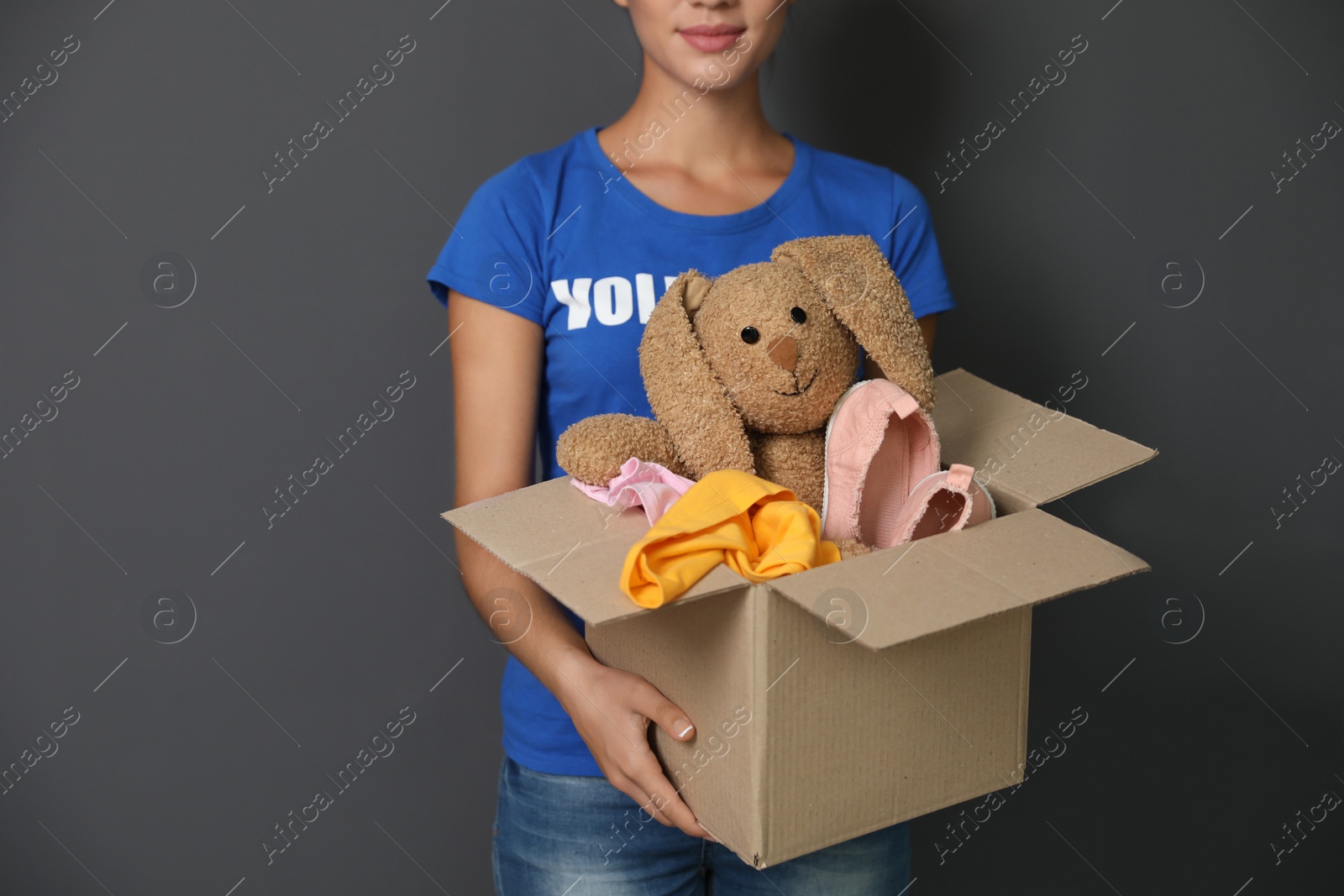 Photo of Female volunteer holding box with donations on grey background