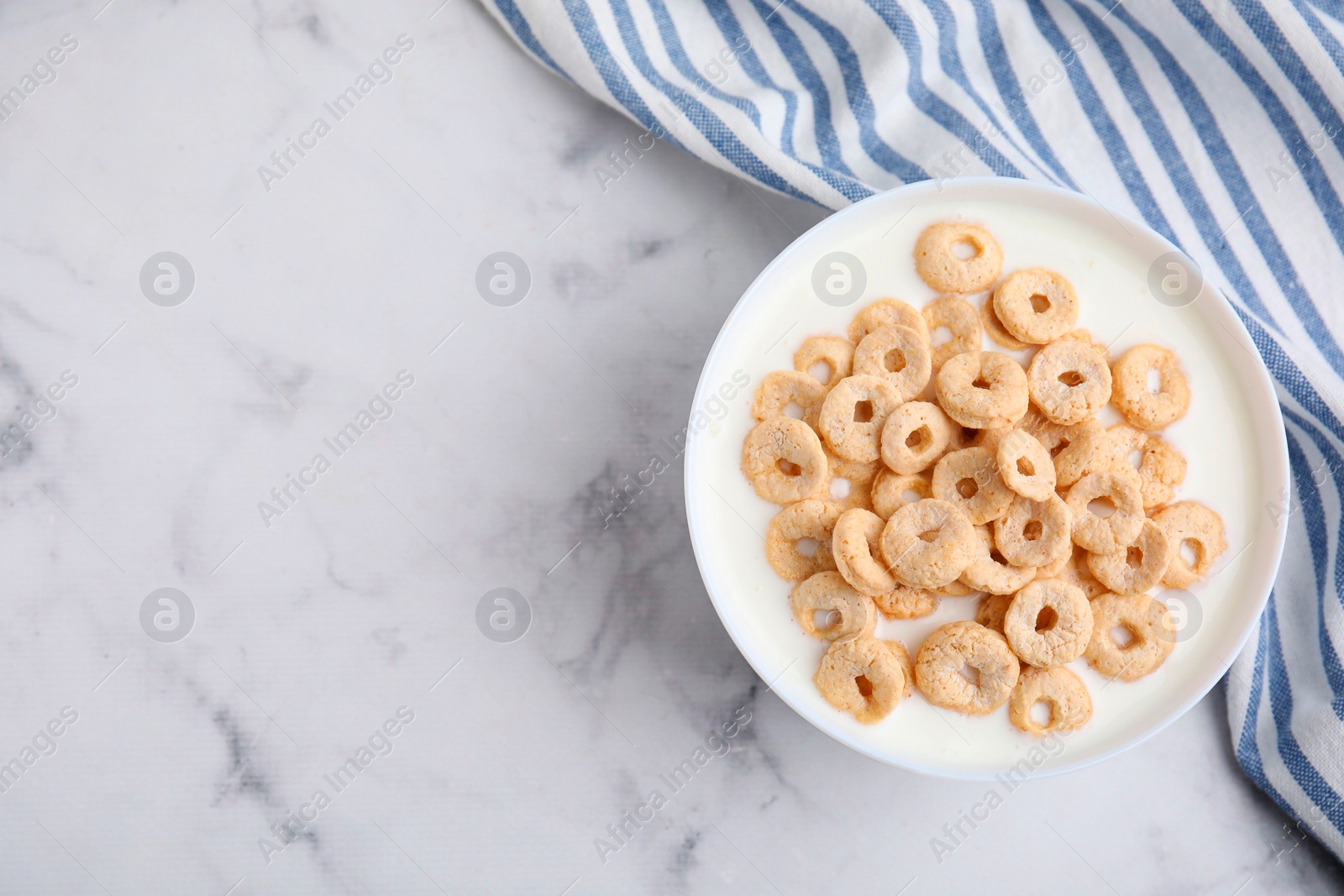 Photo of Breakfast cereal. Tasty corn rings with milk in bowl on white marble table, top view. Space for text