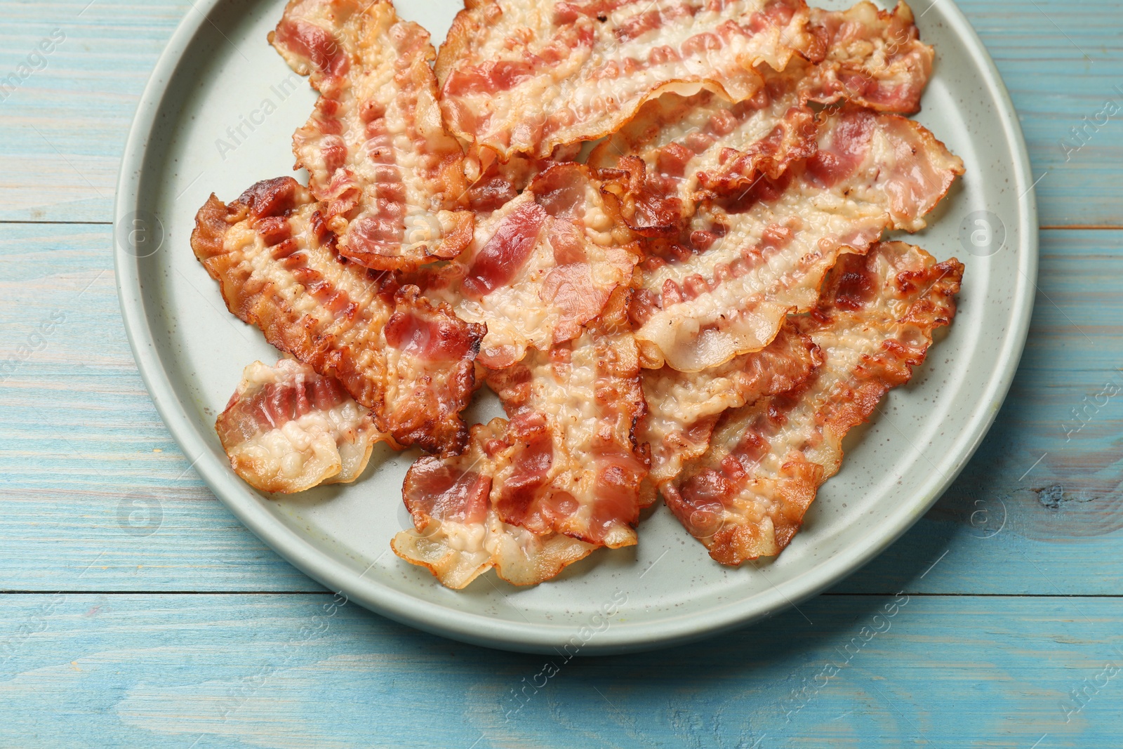 Photo of Delicious fried bacon slices on blue wooden table, top view